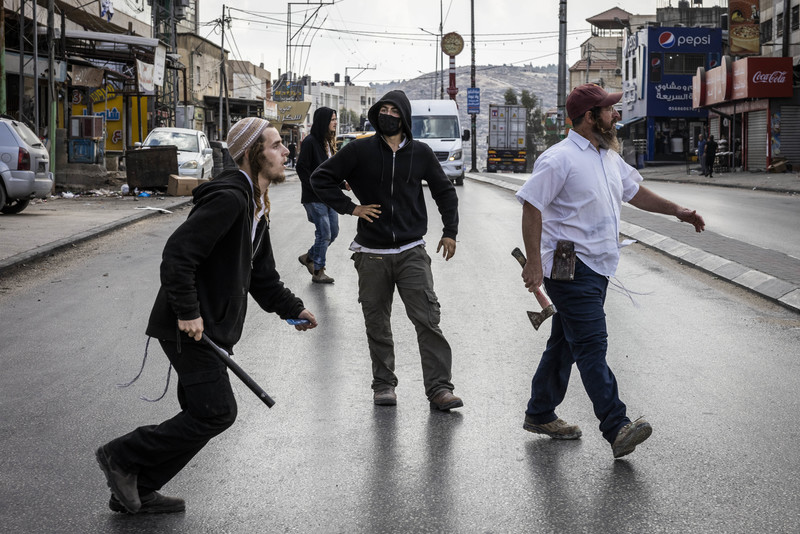 Four settlers armed with sticks and an axe walk down the road in Huwara