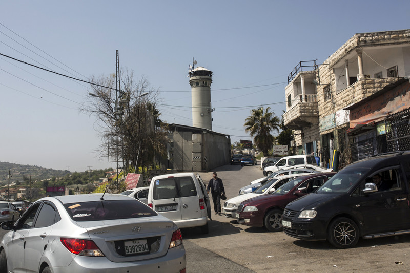 A grey concrete military watchtower hovers over Palestinian traffic