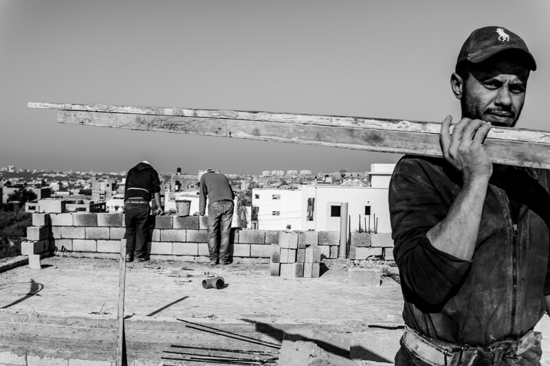 One man carries a wooden beam while two others look over the side of a building