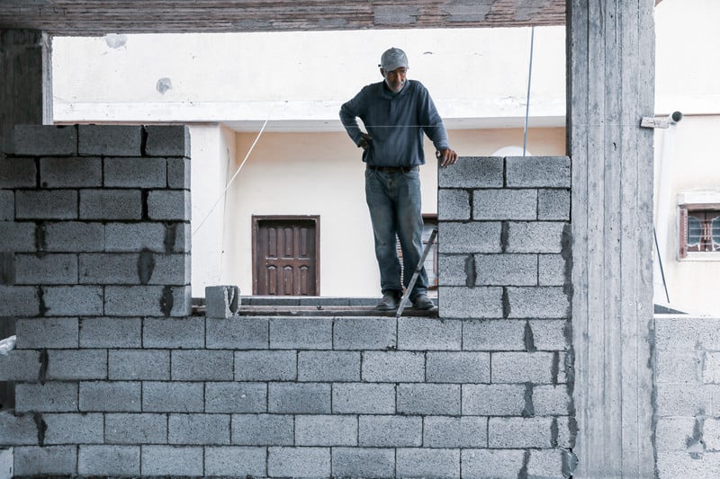 A man stands atop an unfinished brick wall