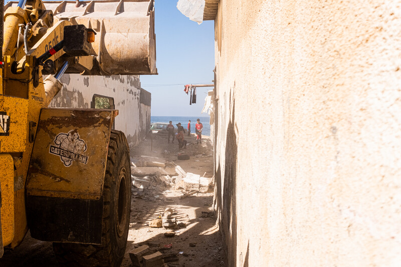 A bulldozer drives down a narrow alley