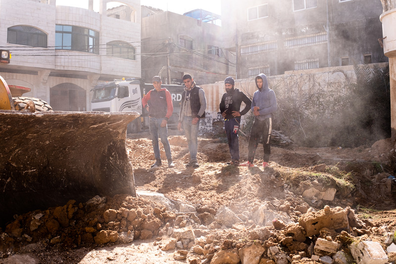 Four men look at rubble as dust rises around them