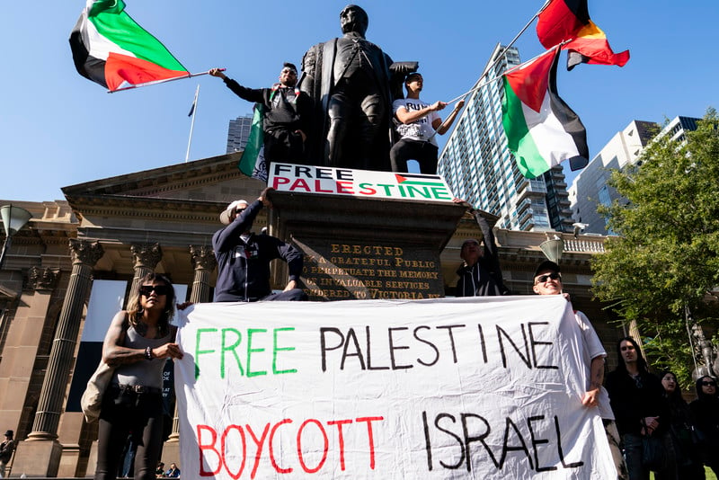 ctivists hold a large free palestine banner and flags in front of a statue and a neo-classical building