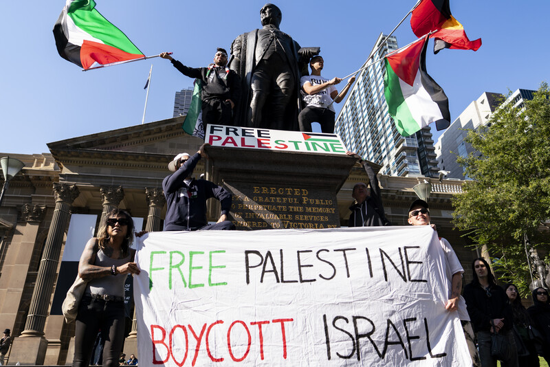 ctivists hold a large free palestine banner and flags in front of a statue and a neo-classical building