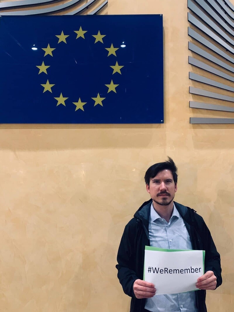 Man standing under EU flag holds sign saying we remember