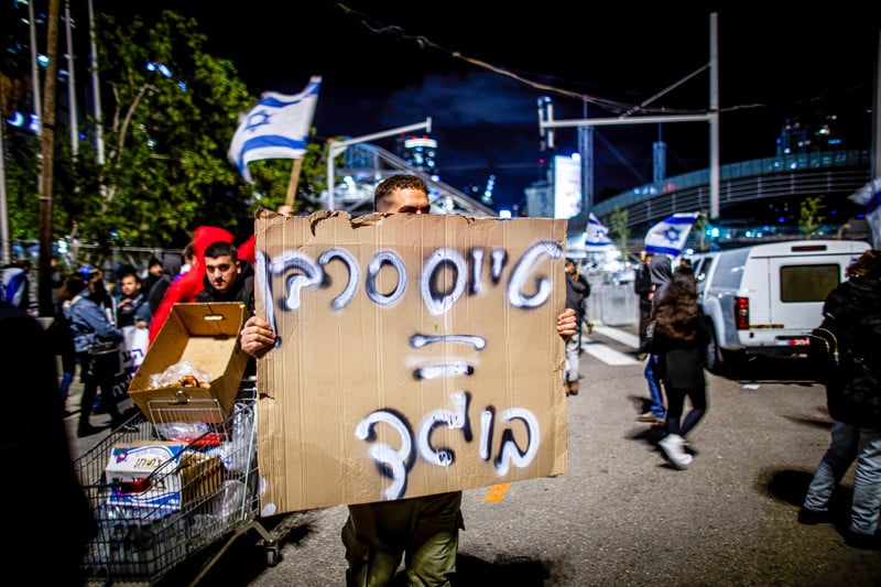A man holds a hand-written sign in Hebrew