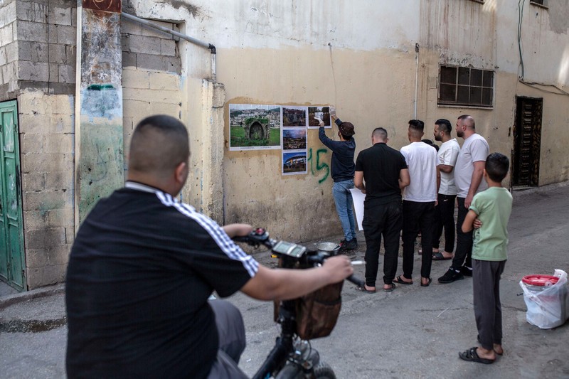 A small crowd gathers around a man plastering photos on a wall