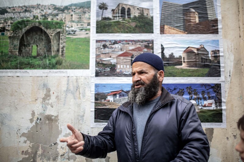 A man gesticulates in front of a wall of photos