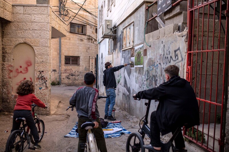 Children on bicycles watch a man plaster posters