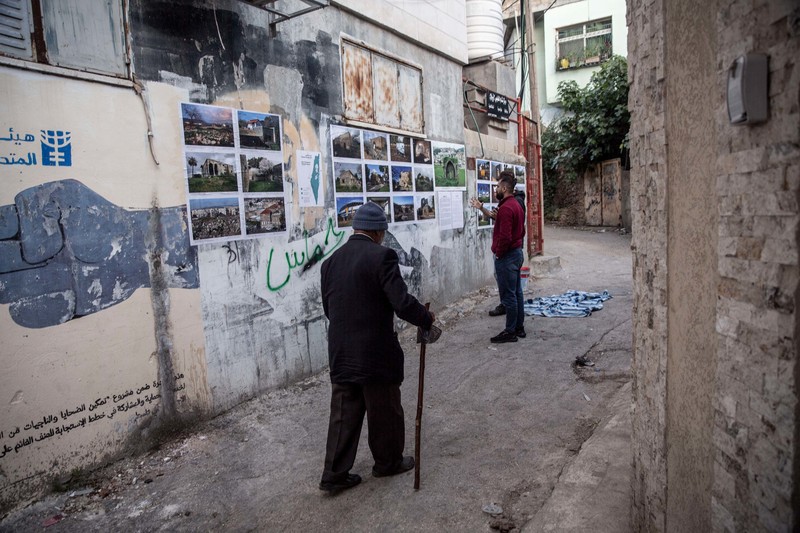 Men walk past a number of photos plastered to a wall