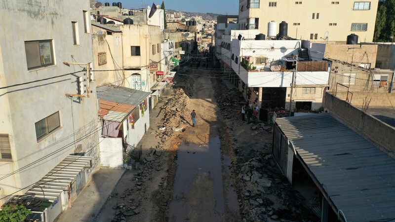 Man seen from above walks along a wide dug-up road with residential buildings on opposite sides