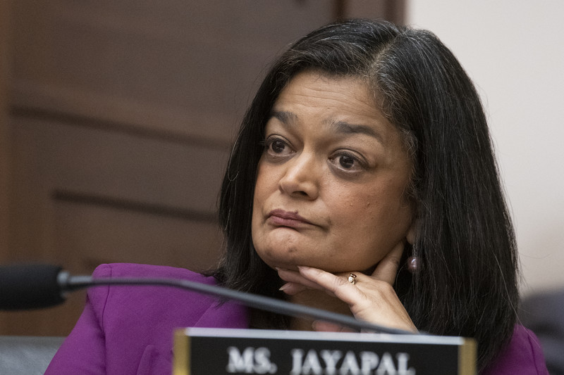 Pramila Jayapal holds her chin in her hands behind a nameplate.