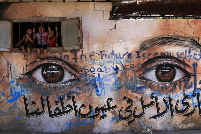 A mural in Gaza city depicts a closeup of realistic eyes as children peek out from a window embedded in the mural