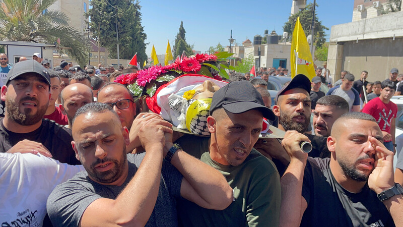 Men carry the corpse of a child on a stretcher, wrapped in flags, during his funeral 