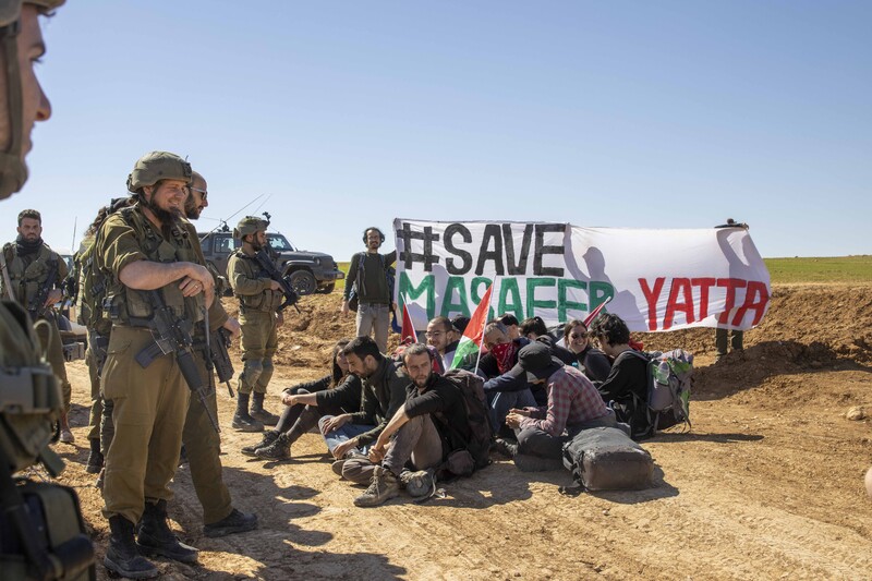 Soldiers surround a group of activists sat on the ground