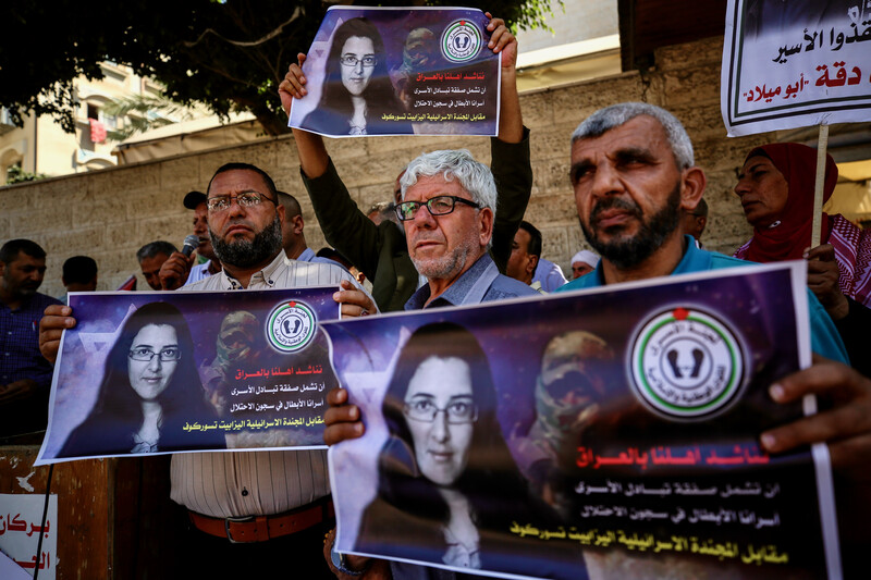 People stand shoulder to shoulder on a sidewalk carrying signs with the face of Elizabeth Tsurkov on them
