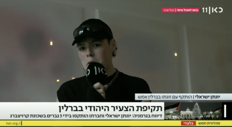 Still from video of man in baseball cap holding microphone speaking to TV news show