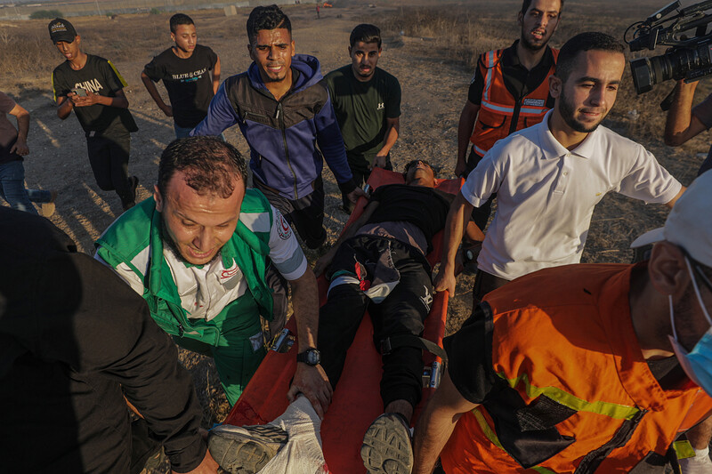 Paramedics and other young men carry man on stretcher with bandaged leg