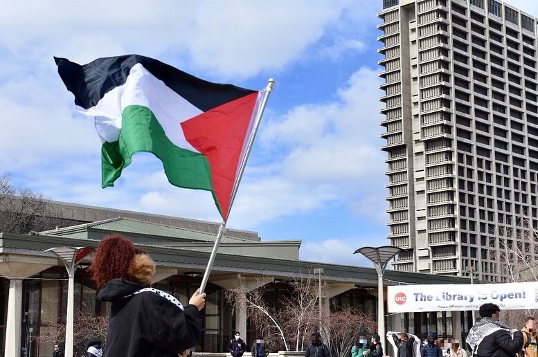 A person holds a Palestinian flag in the courtyard of University of Illinois Chicago.