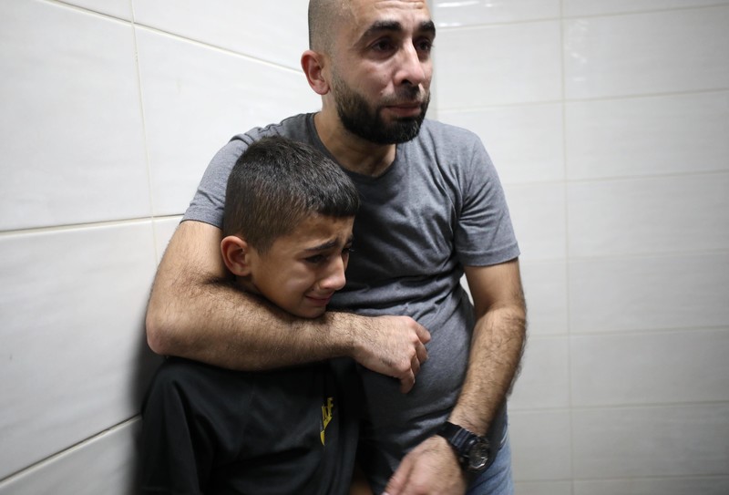 A distressed man has his arm around a child who is crying