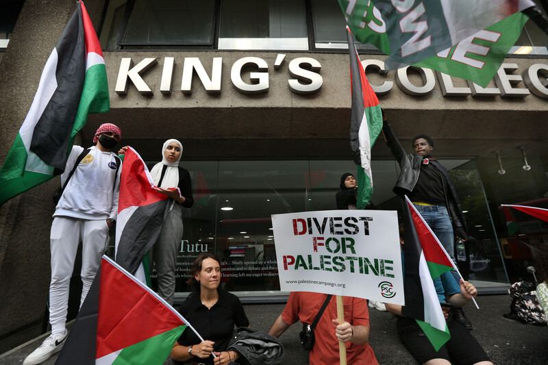 People holding signs and flags appear to be listening to a speaker who is not visible in the picture