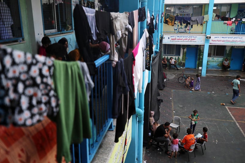Clothing dries from lines hung on balcony as people sit around in small groups in courtyard of school