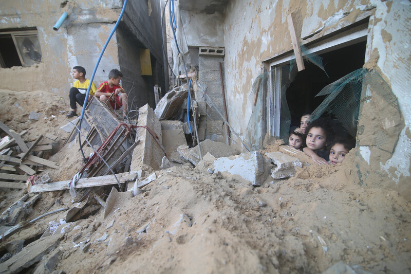 Four young children peer out of a window piled high with rubble in front of it