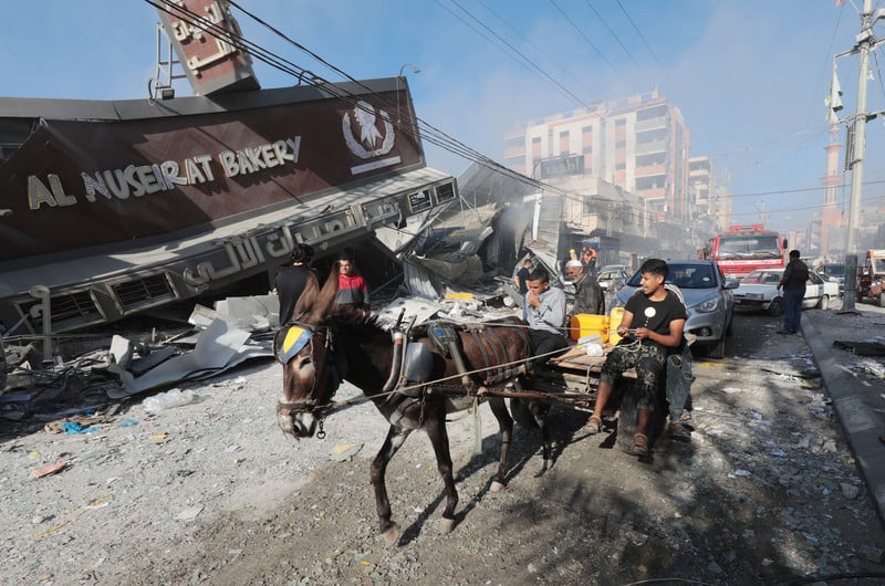 Children on a donkey cart ride past a collapsed building with "Al Nuseirat Bakery" on the front