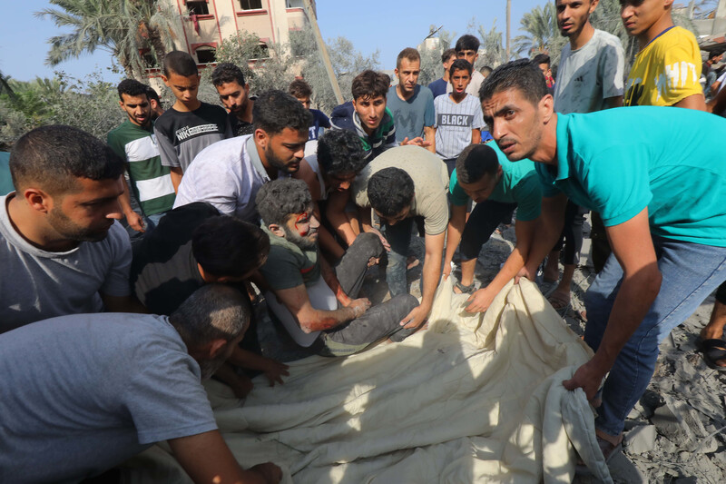 Several hold a blanket on which an injured man is sitting