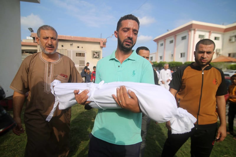 Man holds the body of a child wrapped in cloth 