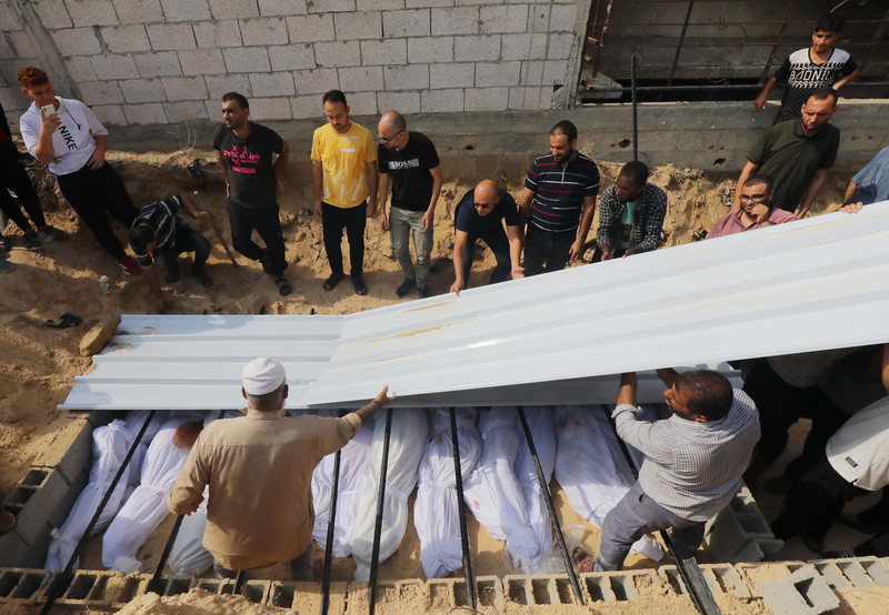 Men lay a plastic sheet over the bodies of several people closely packed together in a shallow grave