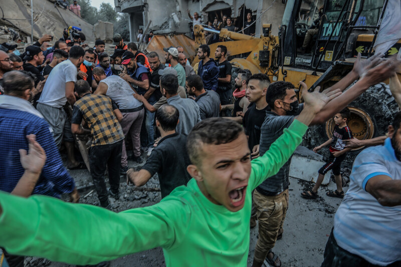 A young man holds his hands in the air while shouting as a group of men are tightly packed behind him