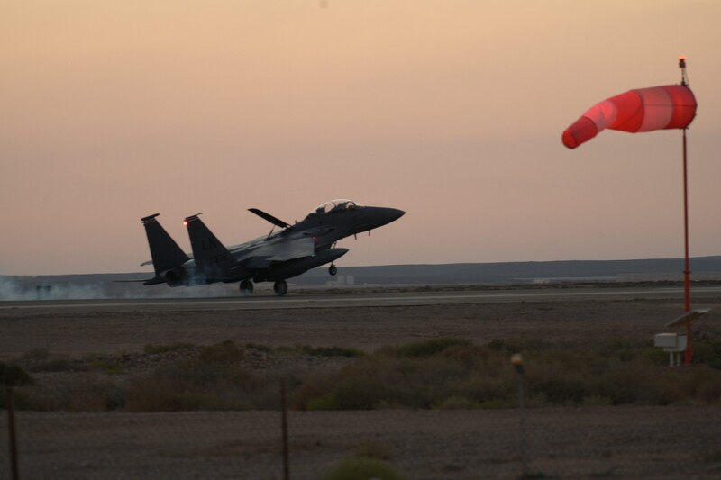 Warplane mid-air appears to be landing in an open field in a dimly lit sky 