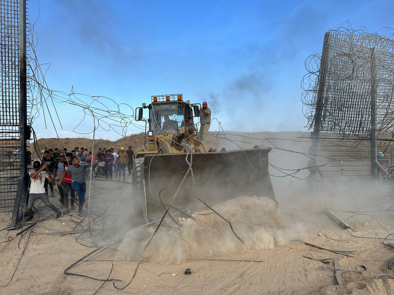 A bulldozer drives through a metal fence