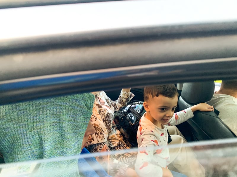 A child and two women with bags sit in the back of a car.