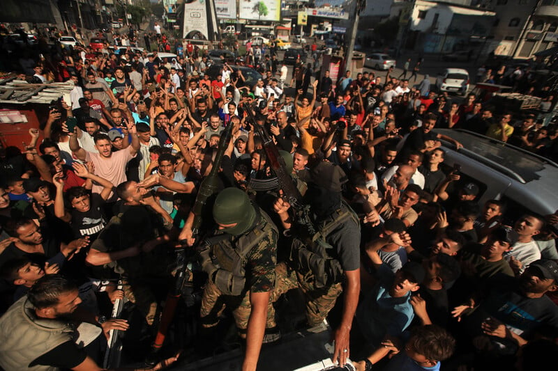 A crowd of young men gather around two men wearing military uniforms and holding guns