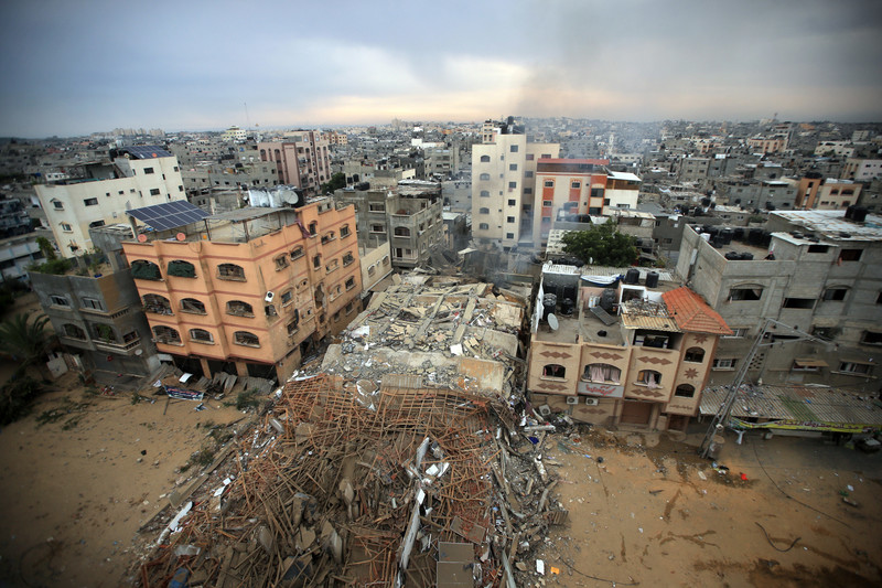 Aerial view of rubble where a building once stood in the middle of two standing and damaged buildings in dense cityscape