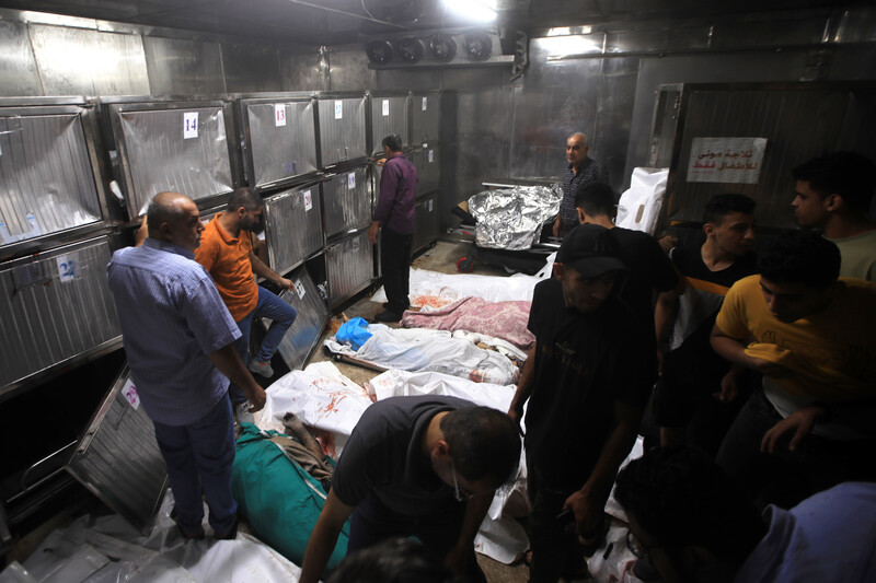 Men stand around bodies wrapped in makeshift shrouds lying on the ground