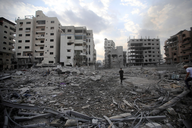 A person walks amid a field of debris surrounded by bombed-out buildings