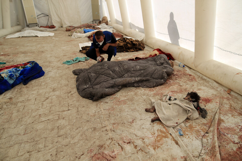 The partially covered body of a toddler lies net to the bodies of adults covered in blankets