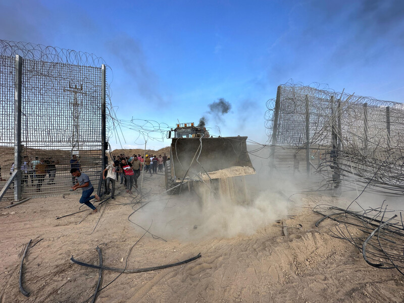 Excavator scoop moves through empty space in fence covered with barbed wire