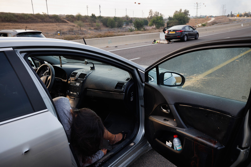 A woman hangs out of the passenger side of a sedan with another car and body seen on a highway