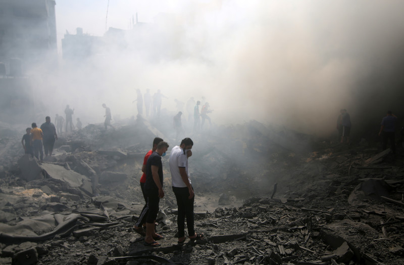 People shrouded in smoke walk through rubble