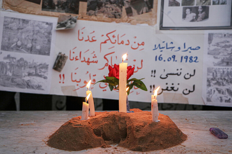 Three lit candles stand before posters remembering the massacres of Palestinians in Lebanon during Israel's invasion which started in 1978 