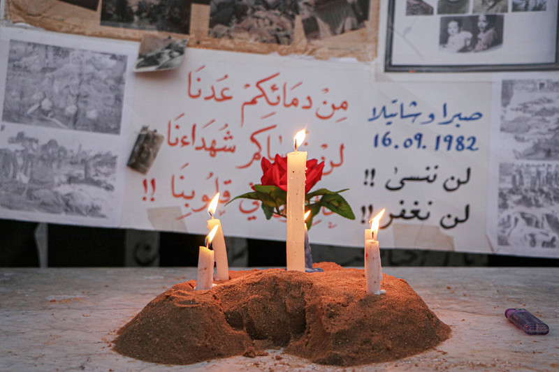 Three lit candles stand before posters remembering the massacres of Palestinians in Lebanon during Israel's invasion which started in 1978 
