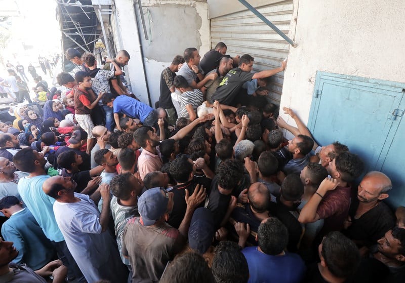 A crowd of men, women and children press up against a partly shuttered bakery