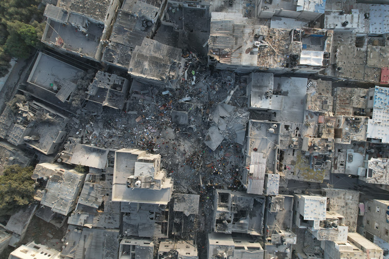 Drone photograph of people standing in the rubble where several buildings once stood in densely built-up area