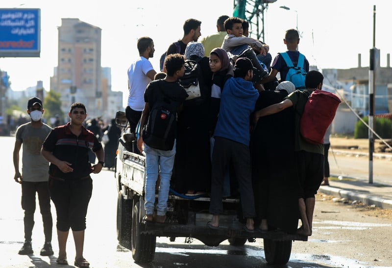 A small truck is seen from the back loaded with men, women and children