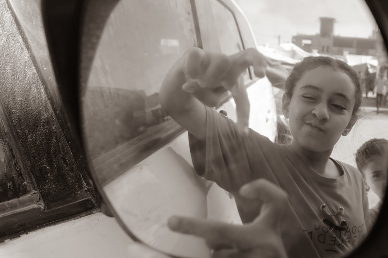 A child poses in the mirror of a car