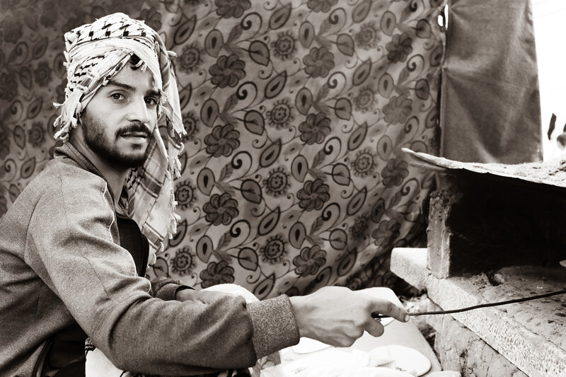 Man looks at camera while taking bread out of clay oven